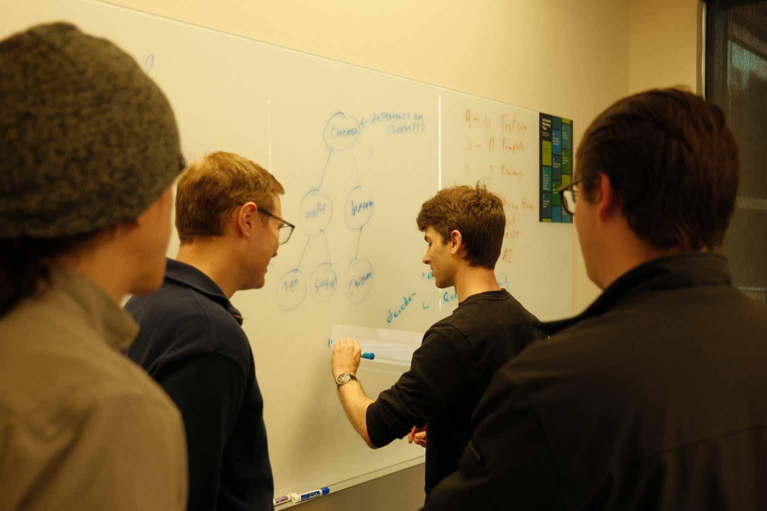 A group of students gathered at a whiteboard, sketching a tree diagram together