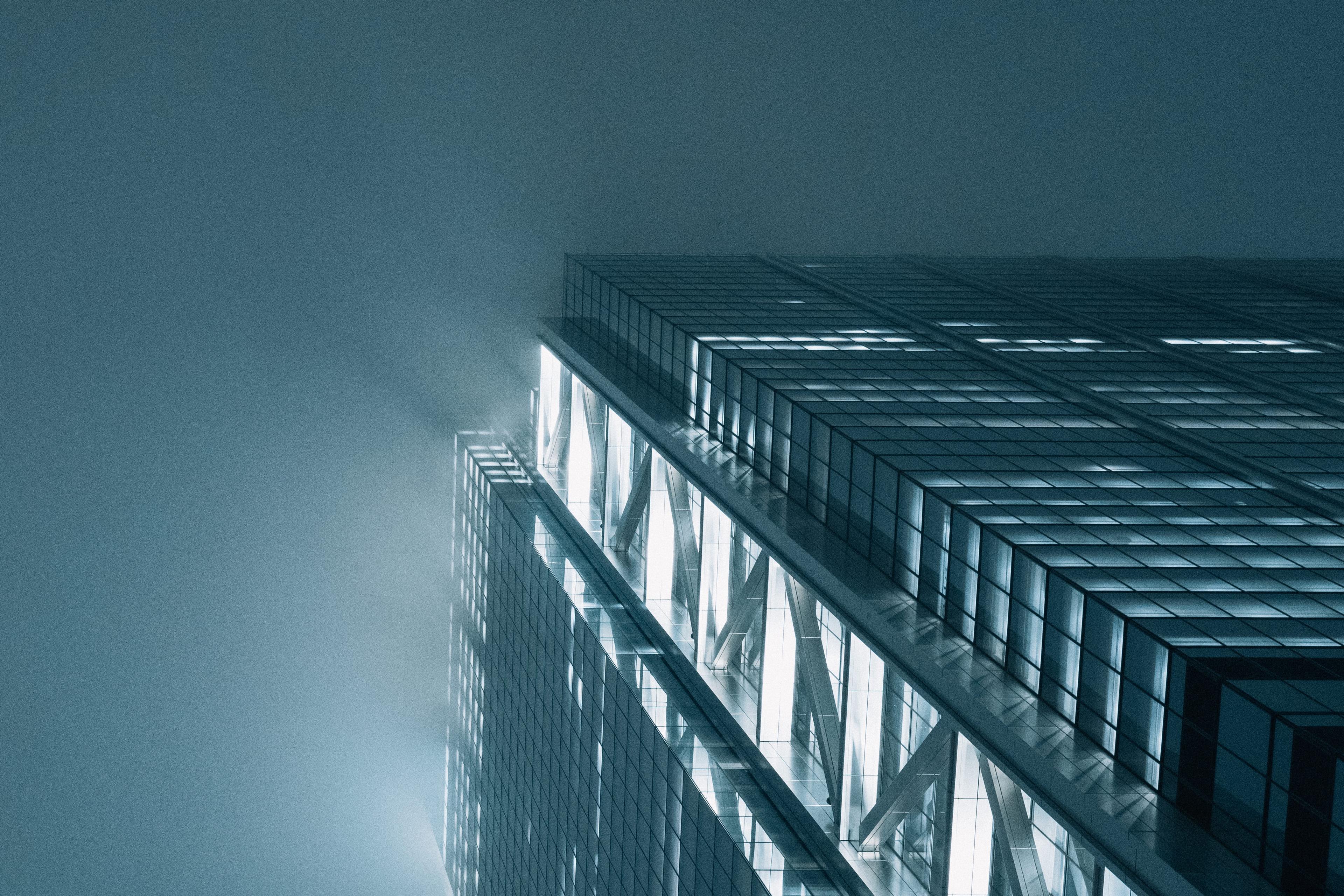 Looking up at a lit glass skyscraper disappearing into fog at night